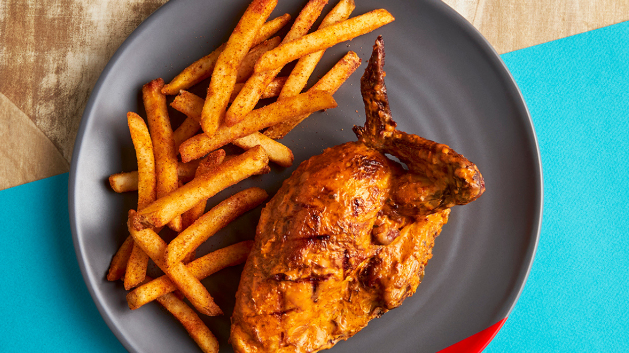 Plate of seasoned French fries served with a piece of spicy roasted chicken on a dark grey dish.