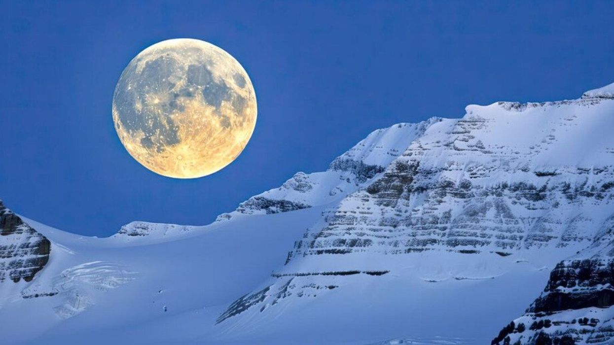 Pleine lune au-dessus d'une montagne enneigée.