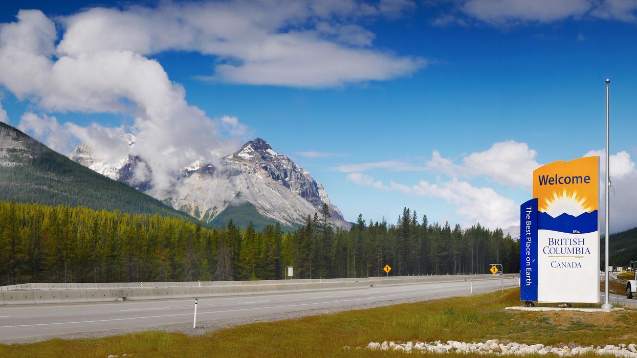 Province of British Columbia sign. by a road besides mountains.