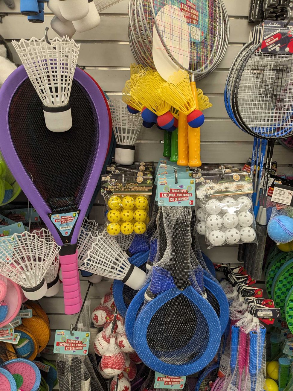 Rackets, birdies, balls, and other sports equipment hanging on a shelf at Dollarama