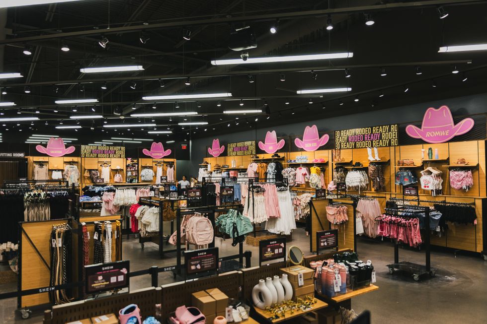 Racks of clothing and tables displaying accessories with signs shaped like pink cowboy hats decorating the walls. 