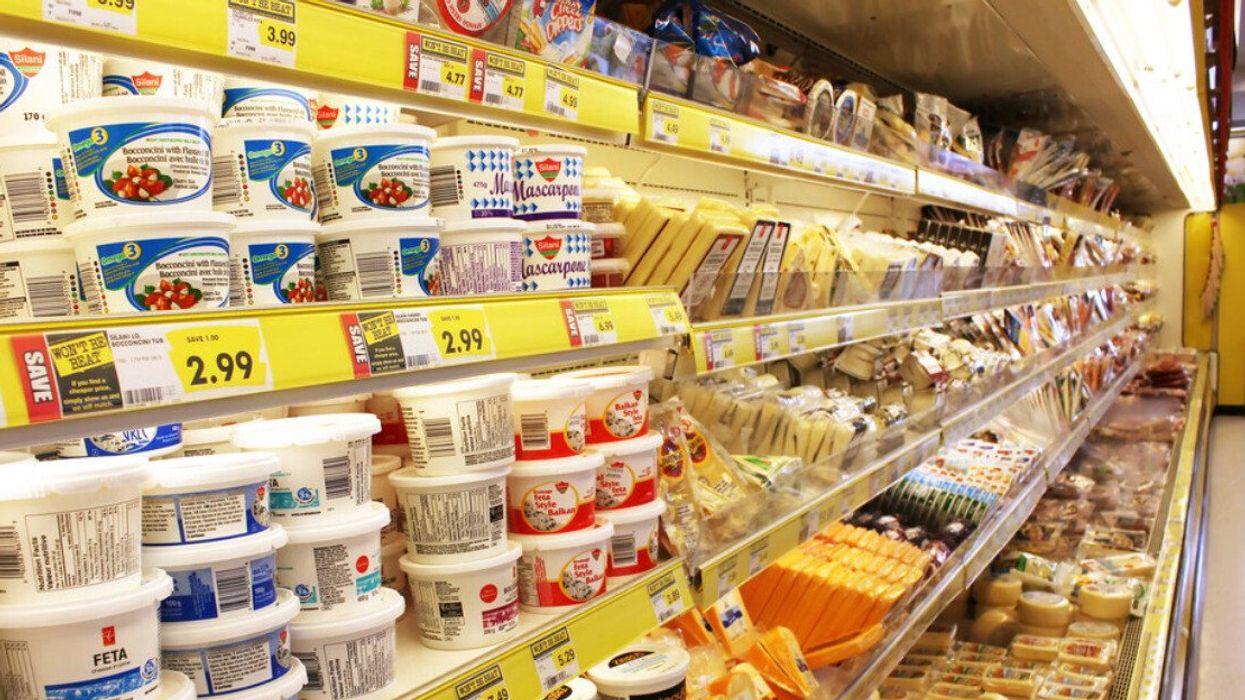 Rangée d'épicerie où se trouve des frigos avec différents produits laitiers, dont du fromage feta et des barres de fromage.