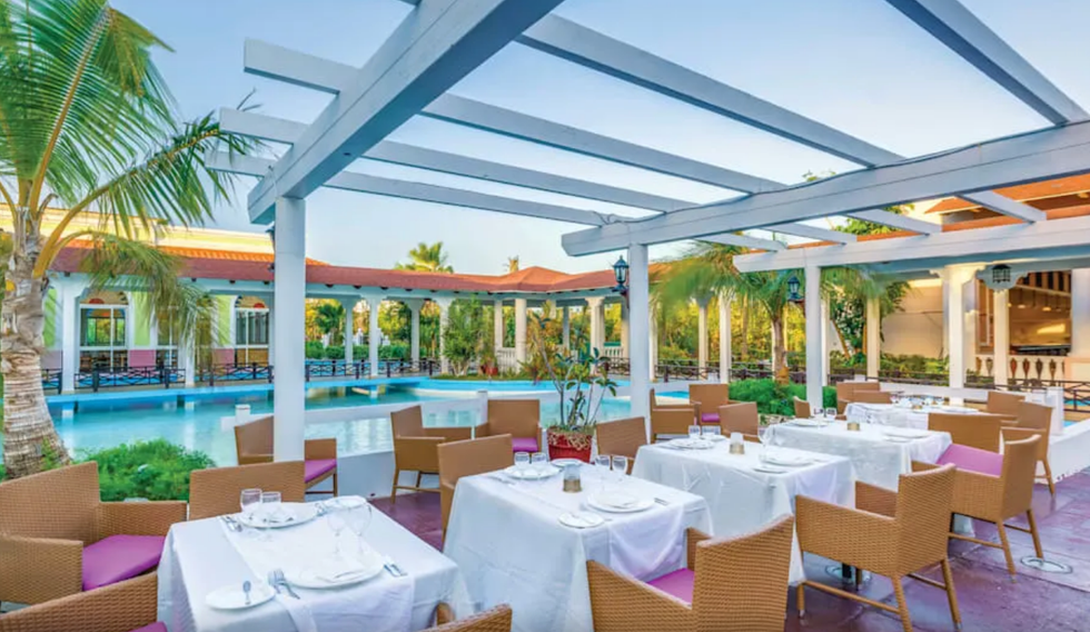 Restaurant sur le bord d'une piscine, entour\u00e9 de palmiers.