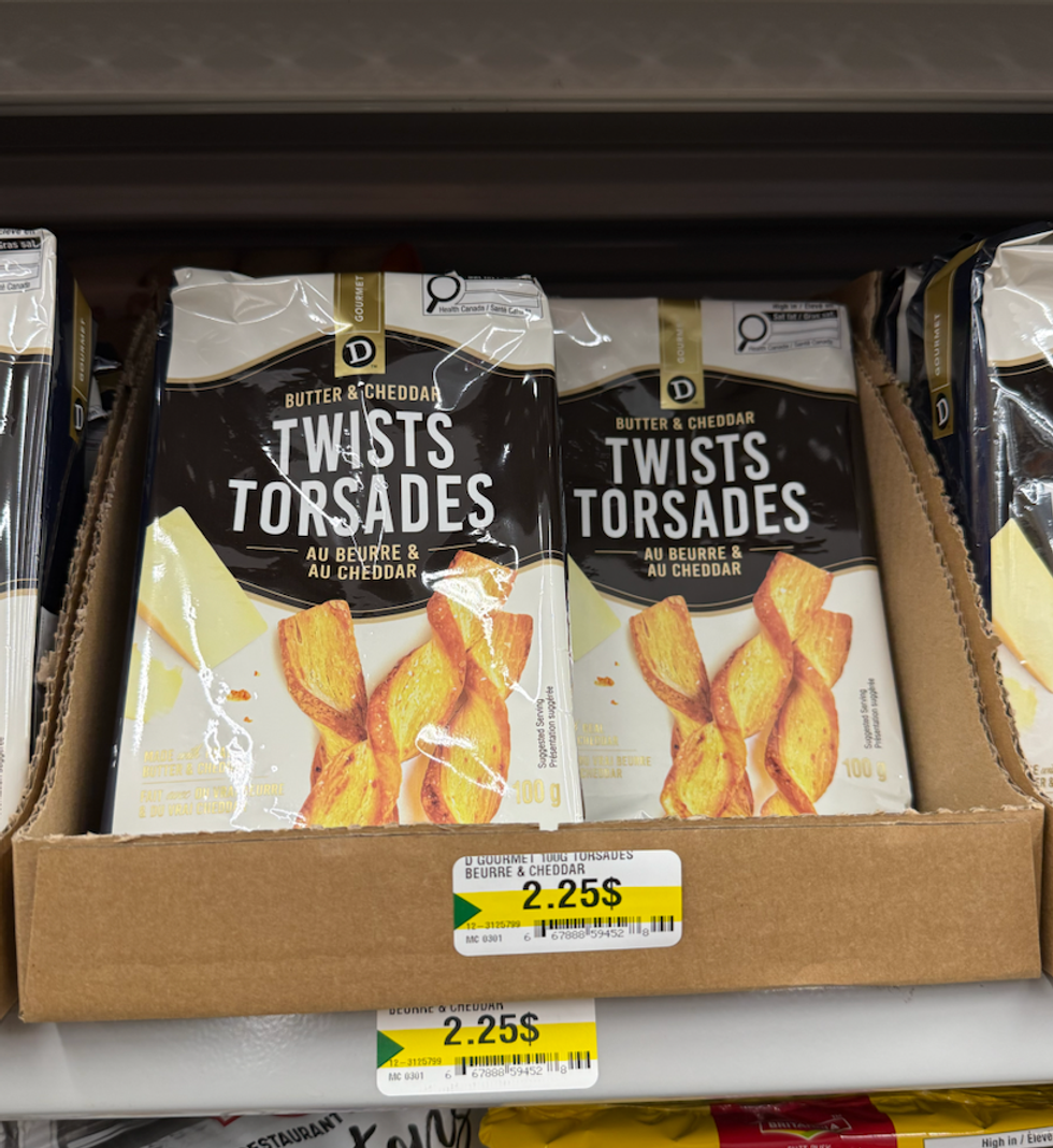 Sacs de torsades au beurre et au cheddar expos\u00e9s dans une bo\u00eete sur une tablette chez Dollarama.