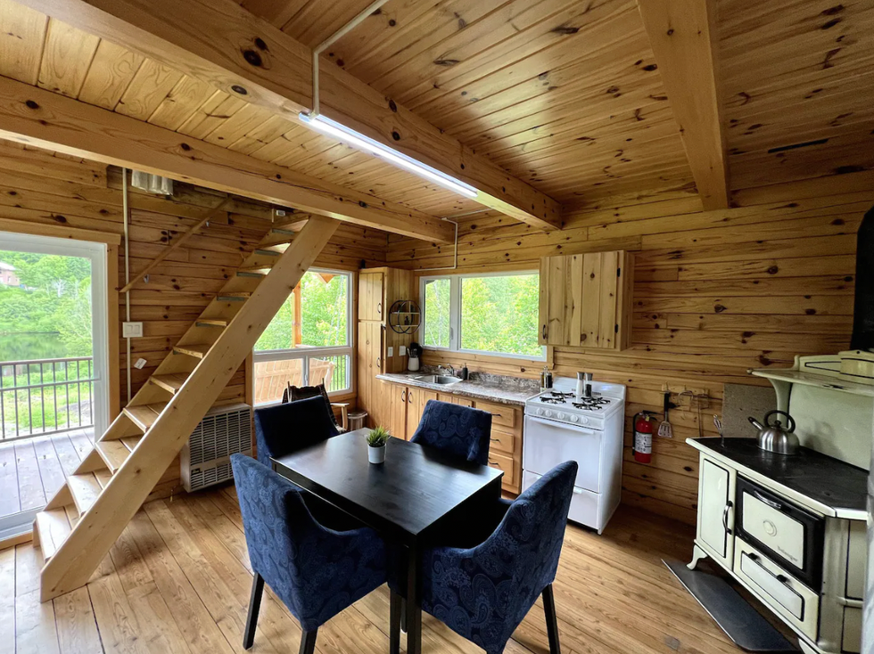 salle \u00e0 manger et cuisine d'un chalet en bois avec les escaliers qui m\u00e8nent \u00e0 l'\u00e9tage