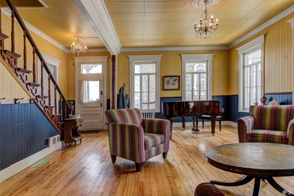 Salon comprenant un piano, deux fauteuils et un escalier vers l'\u00e9tage.