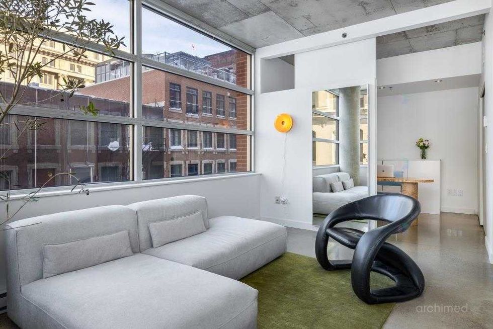 Salon d\u2019angle ultra lumineux avec fen\u00eatres sur deux c\u00f4t\u00e9s, colonne architecturale et design moderne.