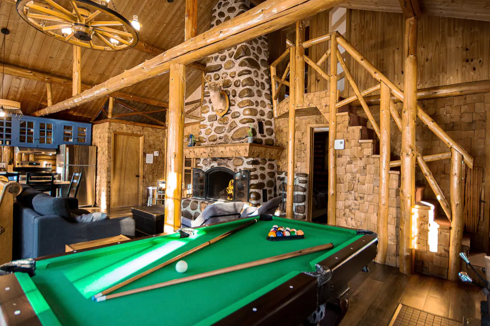 Salon d'un chalet en bois avec un foyer en pierre et une table de billard.