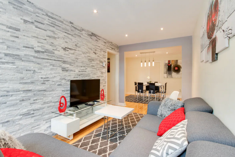 Salon d'un logement avec un canap\u00e9 gris, des coussins rouges et un mur de briques.