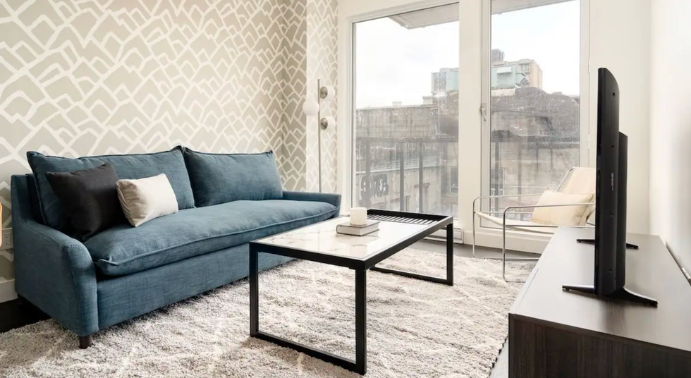 Salon d'un logement avec une baie vitr\u00e9e, un canap\u00e9 et un t\u00e9l\u00e9viseur.