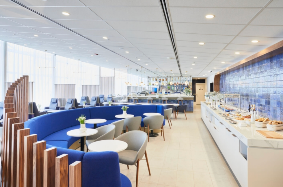 Salon priv\u00e9 avec canap\u00e9 bleu, fauteuils gris, tables blanches et buffet.