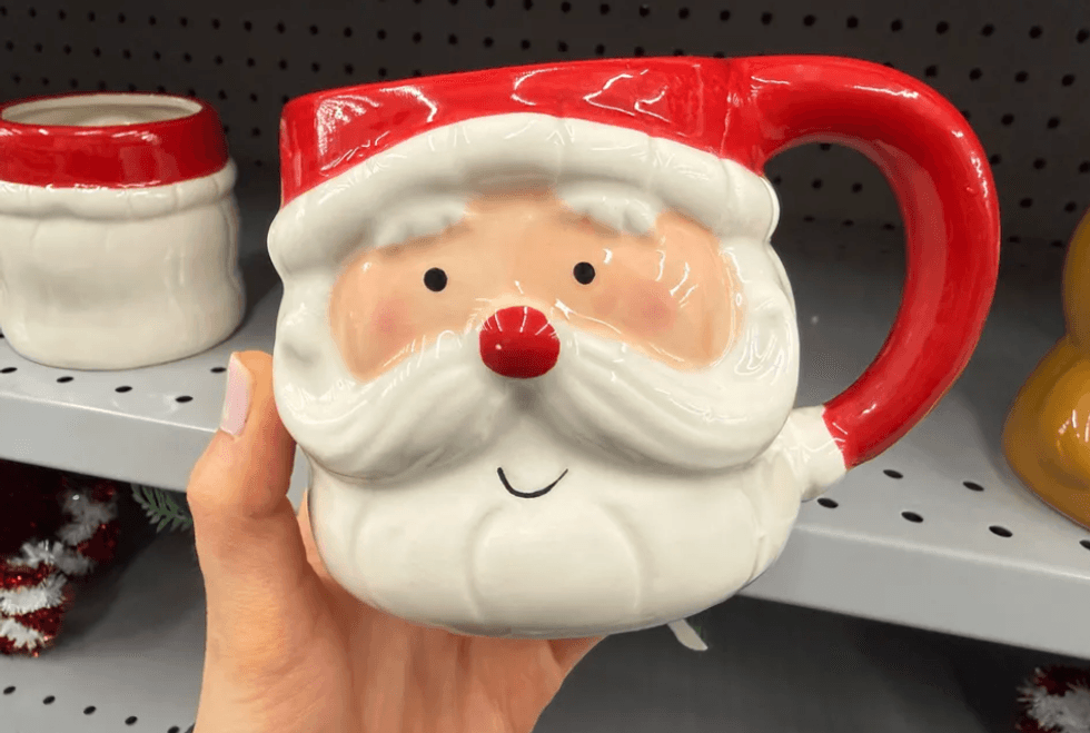 Santa Claus-themed mug with red handle held in hand.