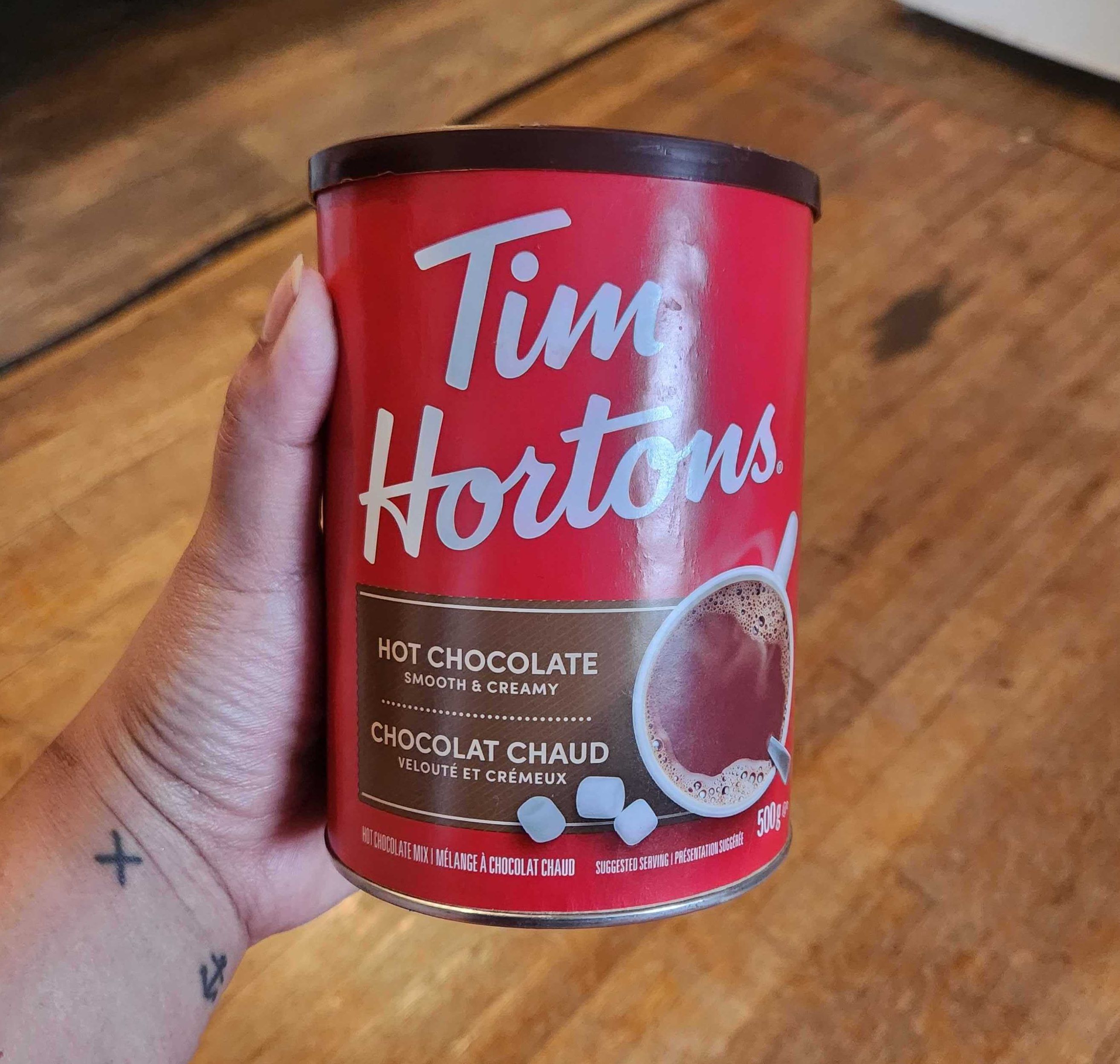 Sarah holding a tin of Tim Hortons hot chocolate from No Frilss, $5.99 for 500 grams.