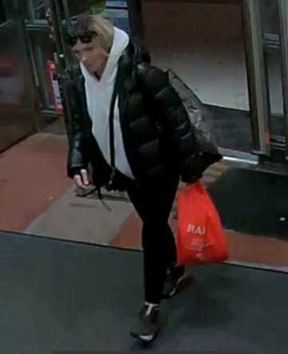 Security camera image of a person with blonde hair in black clothing entering a store.