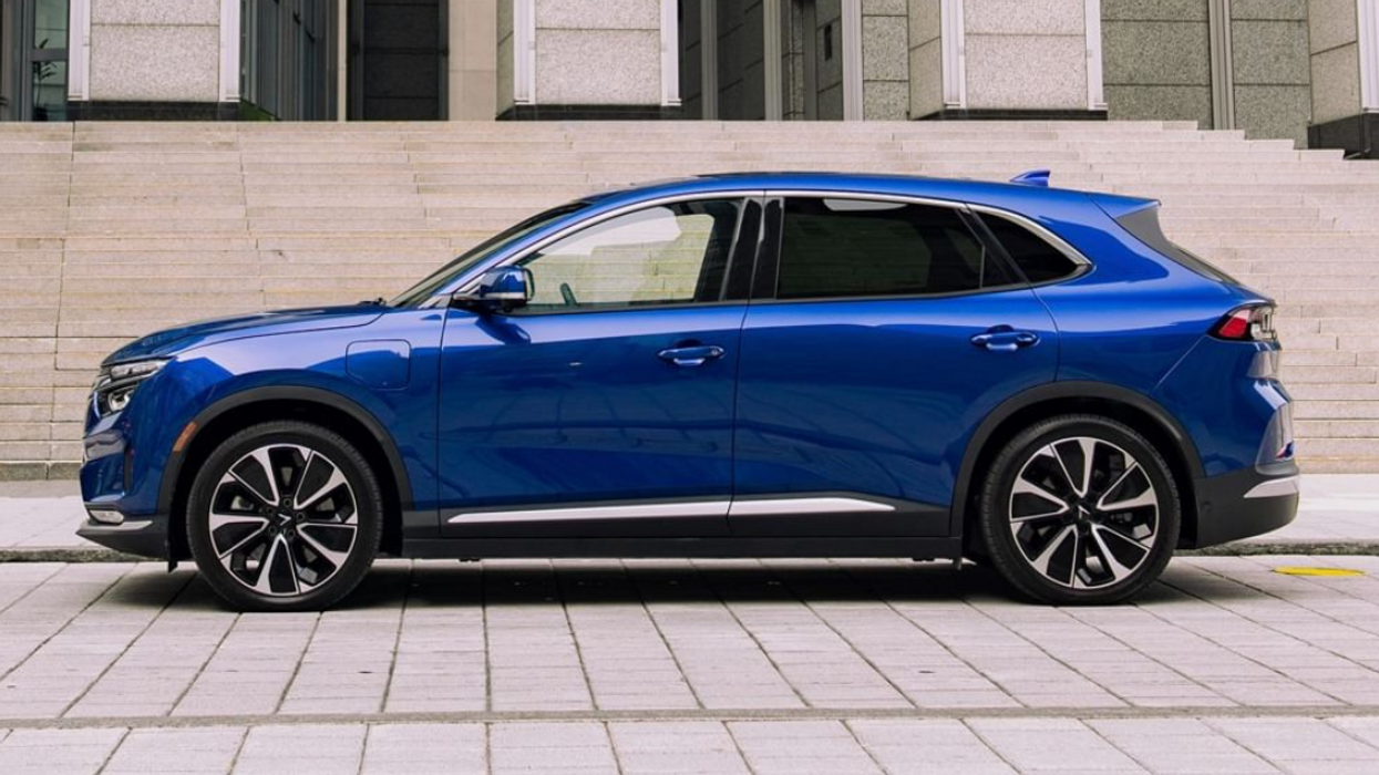Side view of a blue VinFast VF 8 SUV parked on a paved street in front of a grey cement building.