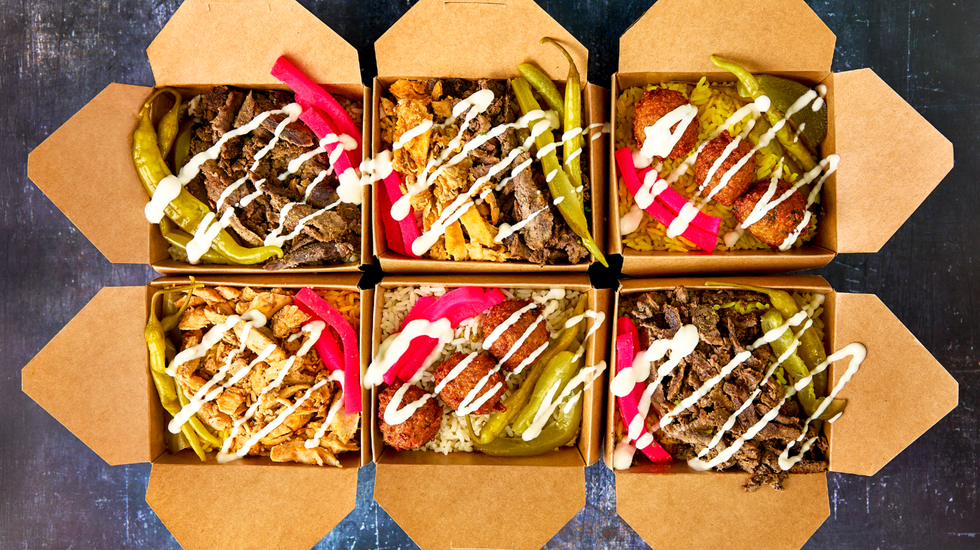 Six takeout food boxes filled with an assortment of pickles, falafel, rice, shawarma and sauce.