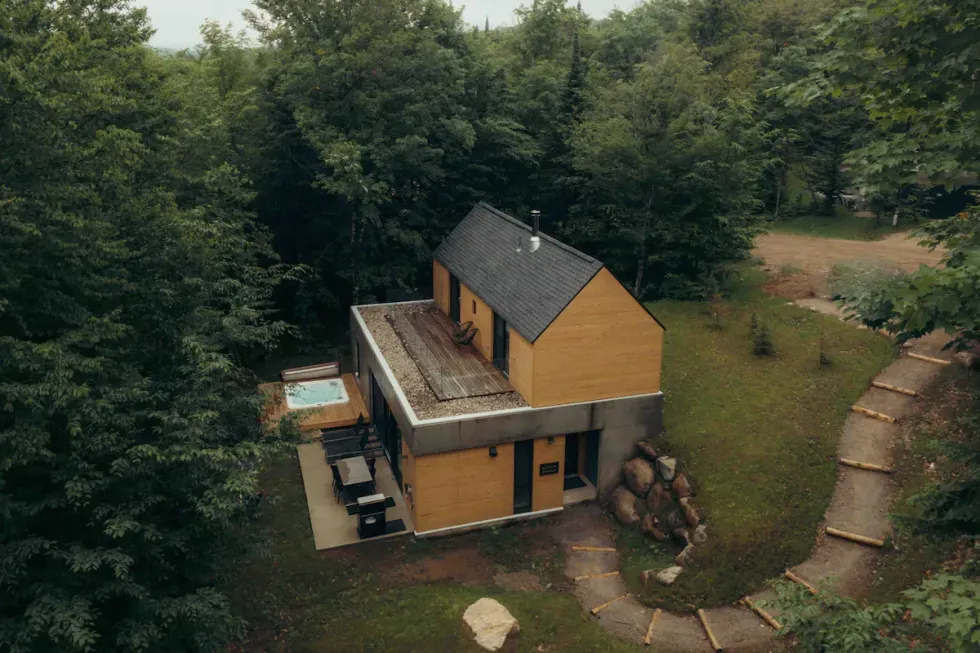 Sleek two-storey wooden cabin with a spacious deck and outdoor hot tub.