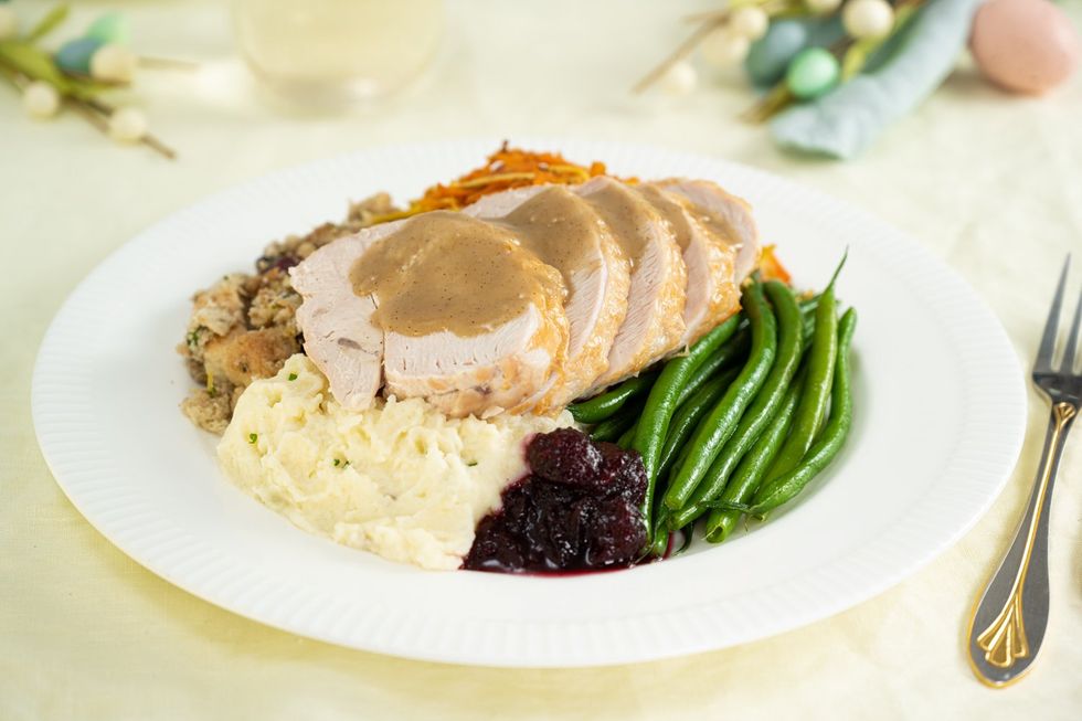 Sliced pieces of turkey on a plate with beans, cranberry sauce, mashed potatoes and stuffing.