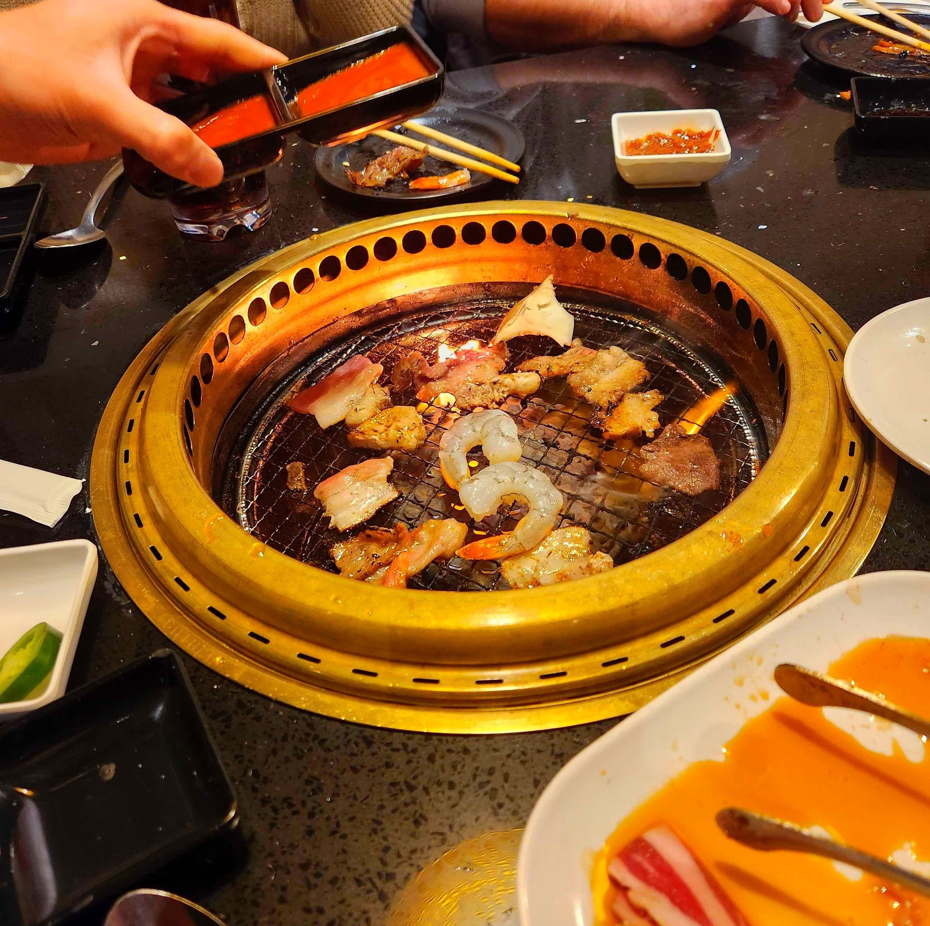 Small plates of food on a table and food cooking on a grill at Gyubee.