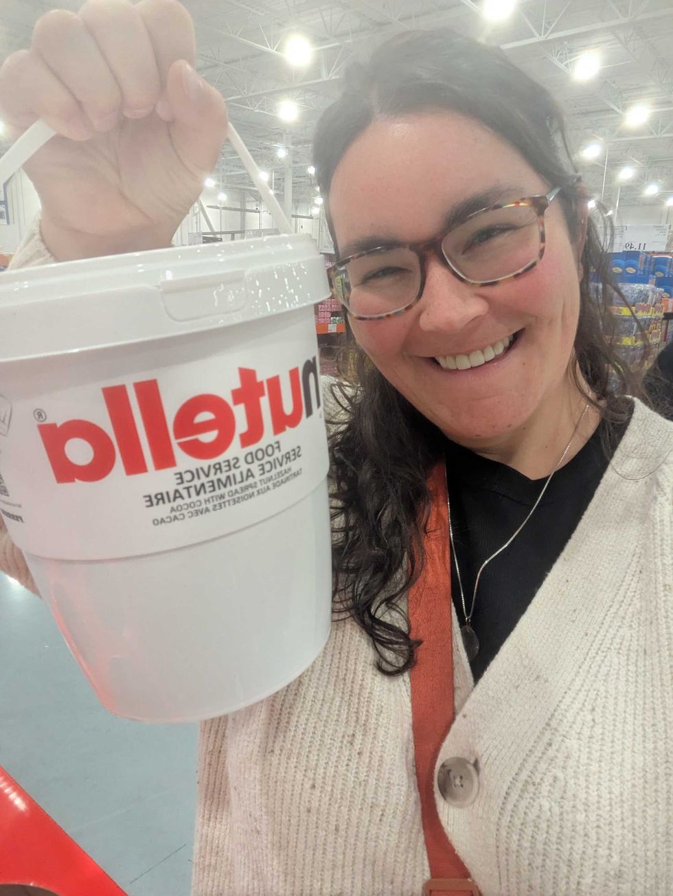 Smiling woman holding a large Nutella container in a store aisle