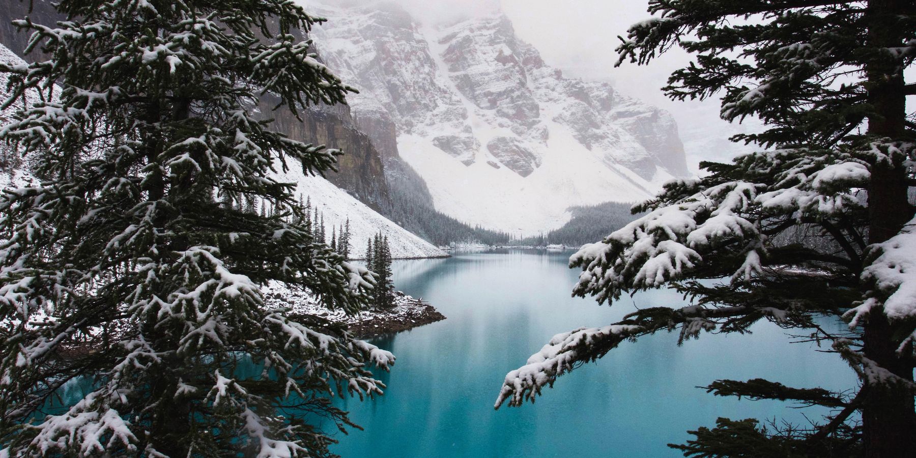Snow-covered conifers, mountains and a frozen lake.