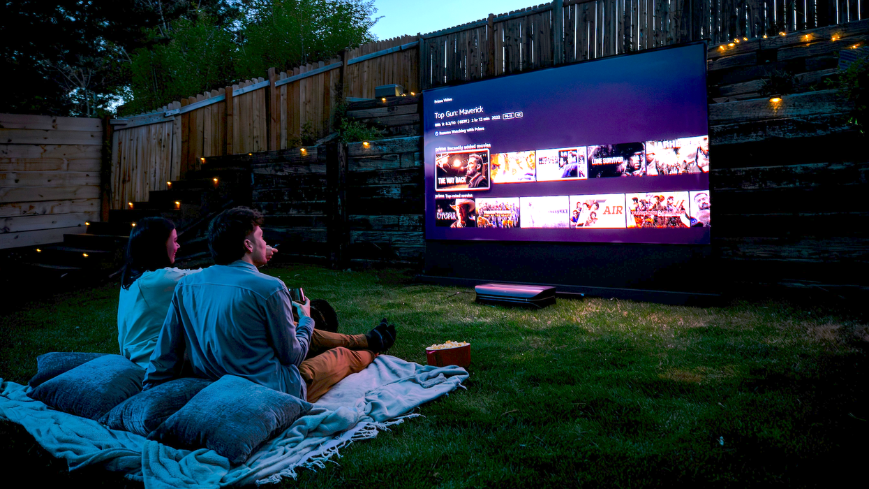 Soirée cinéma en plein air avec projecteur et grand écran dans une cour aménagée, couple sur couverture