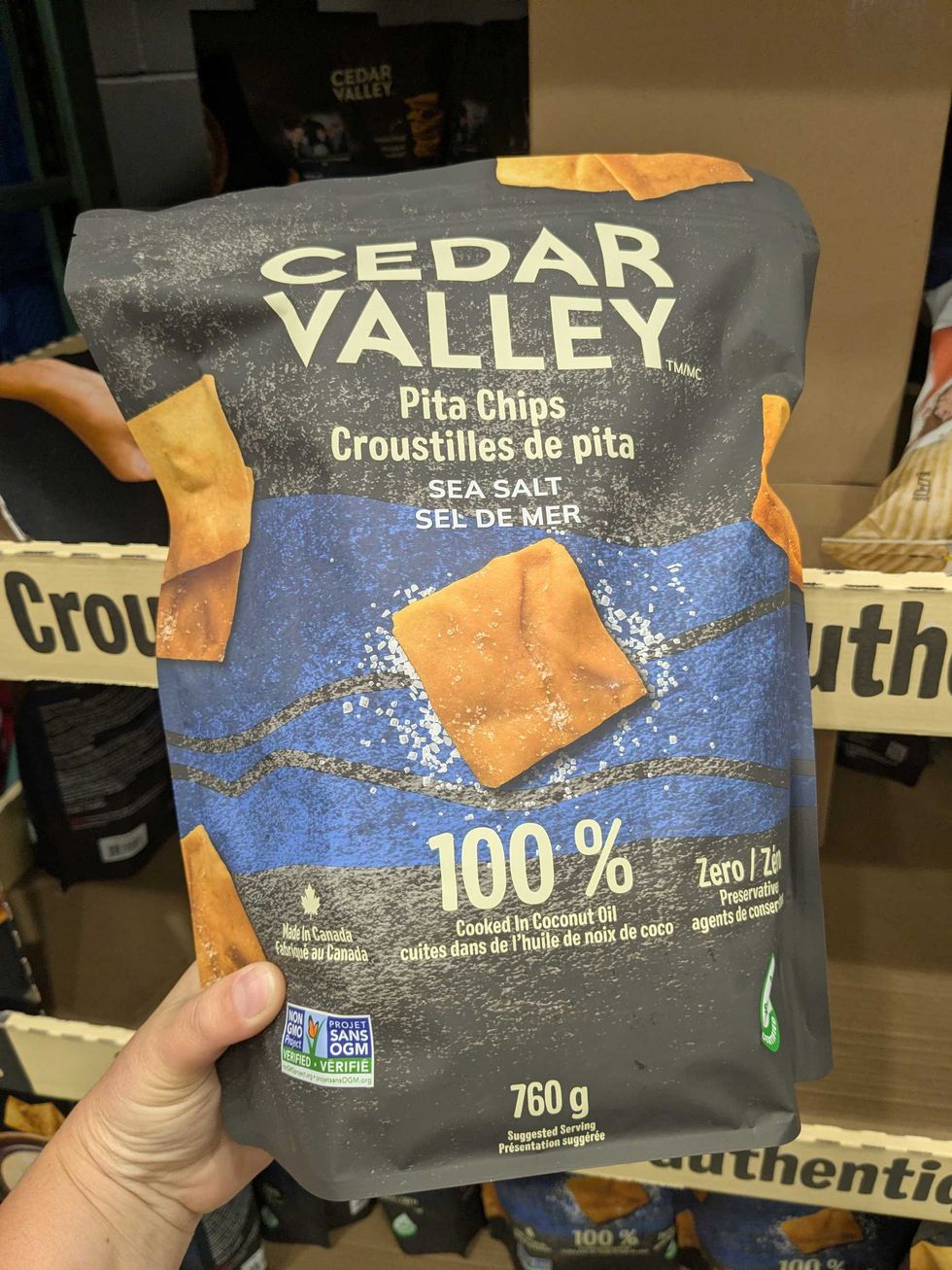Someone holding a bag of Cedar Valley pita chips in front of a Costco shelf