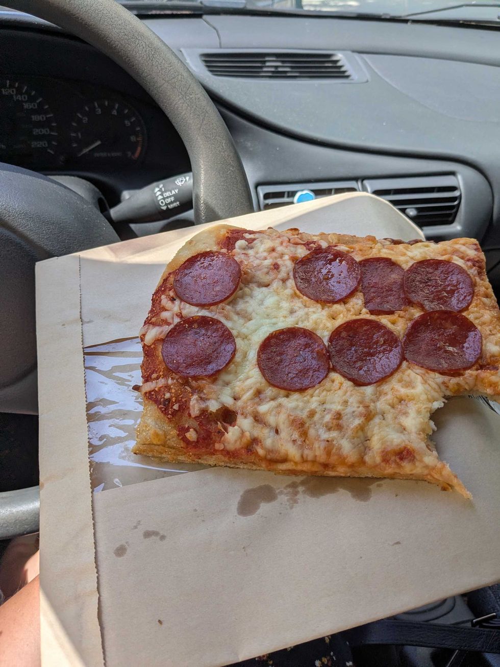 Someone holding a brown bag with a square slice of pepperoni pizza on it