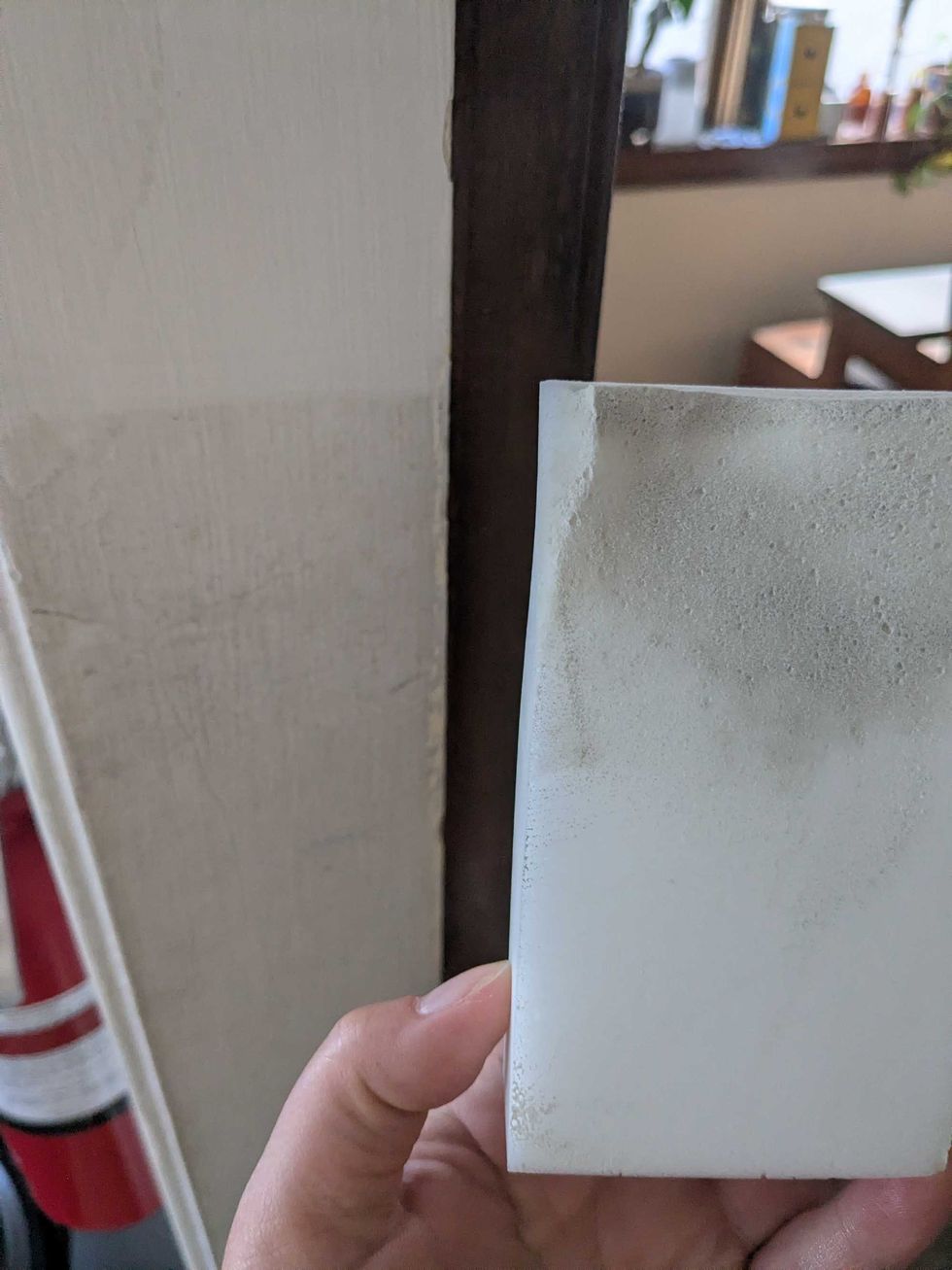 Someone holding a cleaning sponge beside a doorframe that's visibly cleaner