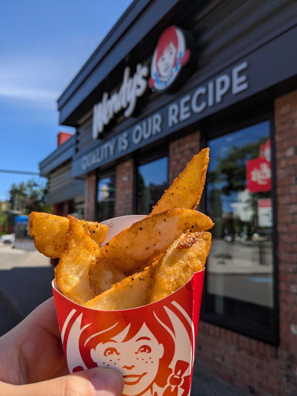 Someone holding a container of fried potatoes up in front of a Wendy's