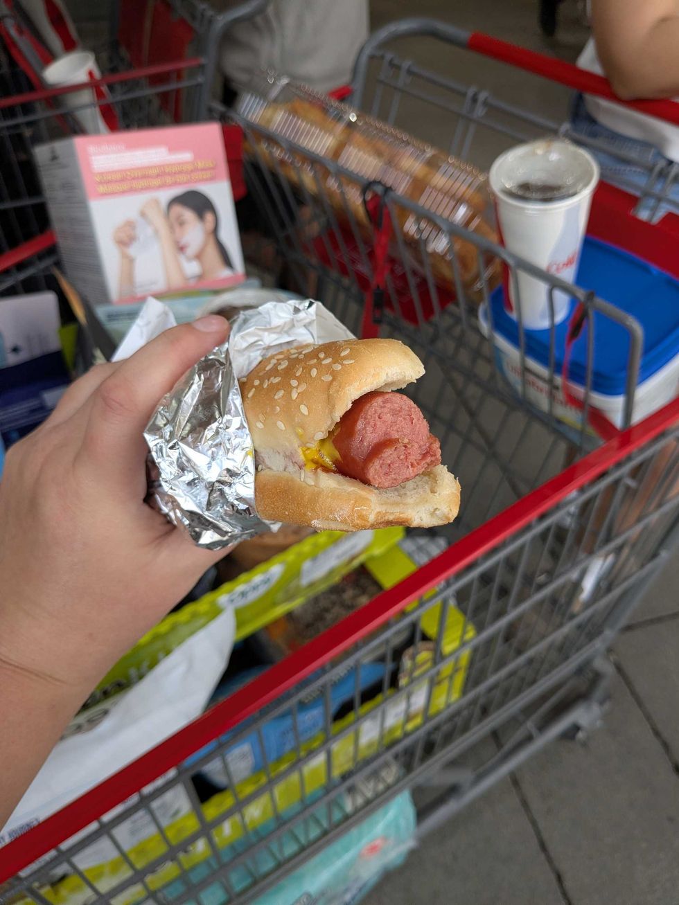 Someone holding a Costco hot dog in front of their shopping cart