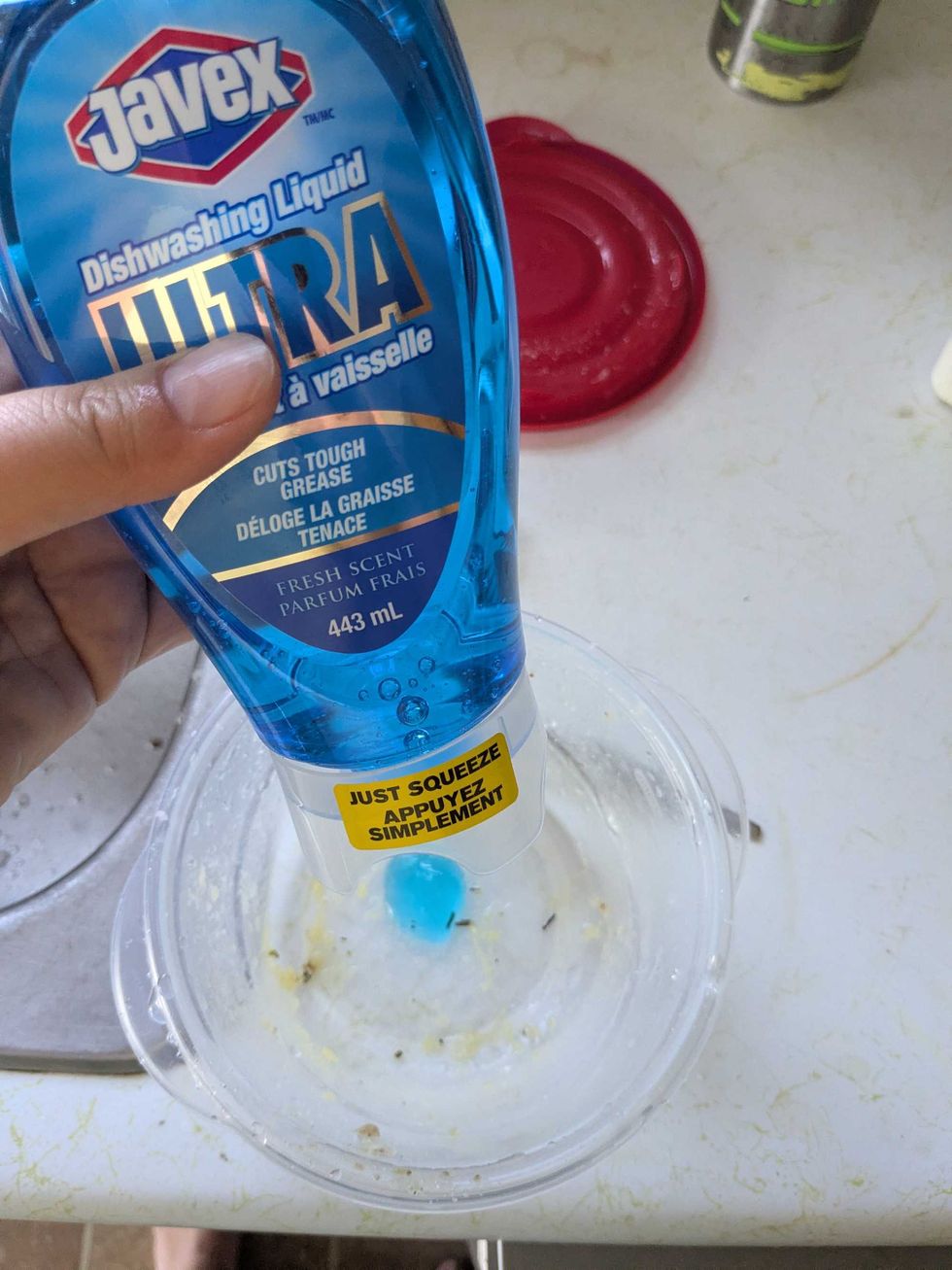 Someone holding a Javex brand dish soap over a dirty container