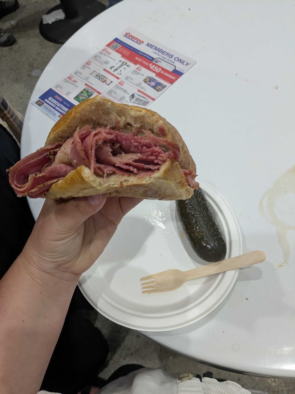 Someone holding a Montreal smoked meat sandwich in front of a table at Costco