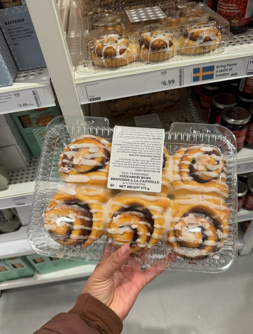 Someone holding a pack of six IKEA cinnamon buns in a plastic box in IKEA.