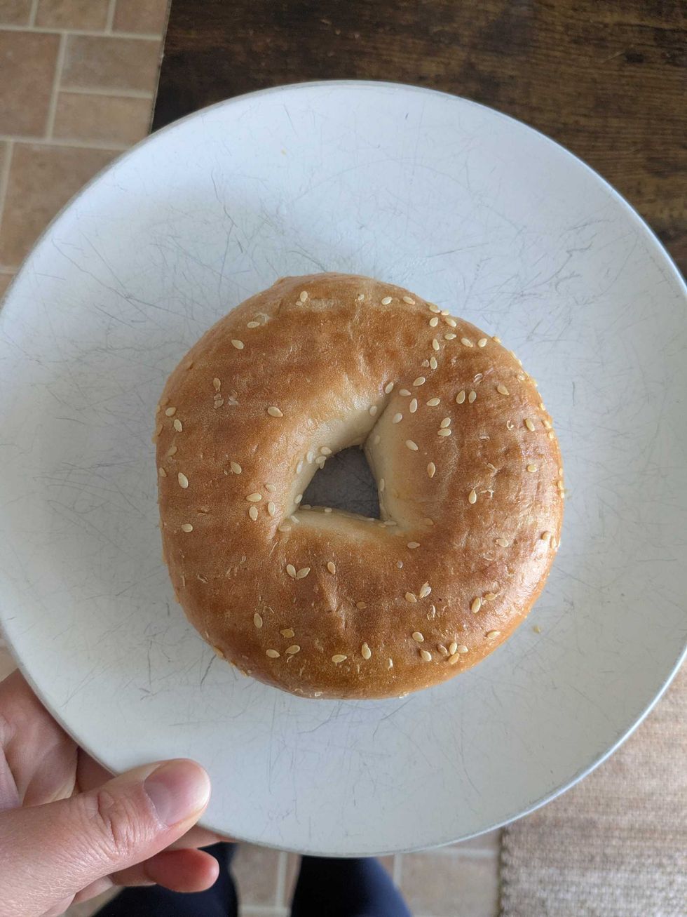 Someone holding a plate with a sesame-seed bagel on it