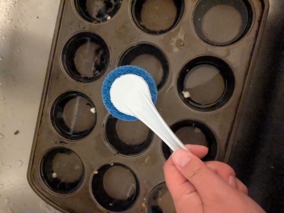 Someone holding a round scrubber in front of a muffin tin