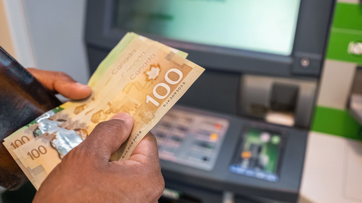 Someone holding Canadian money in front of an ATM.