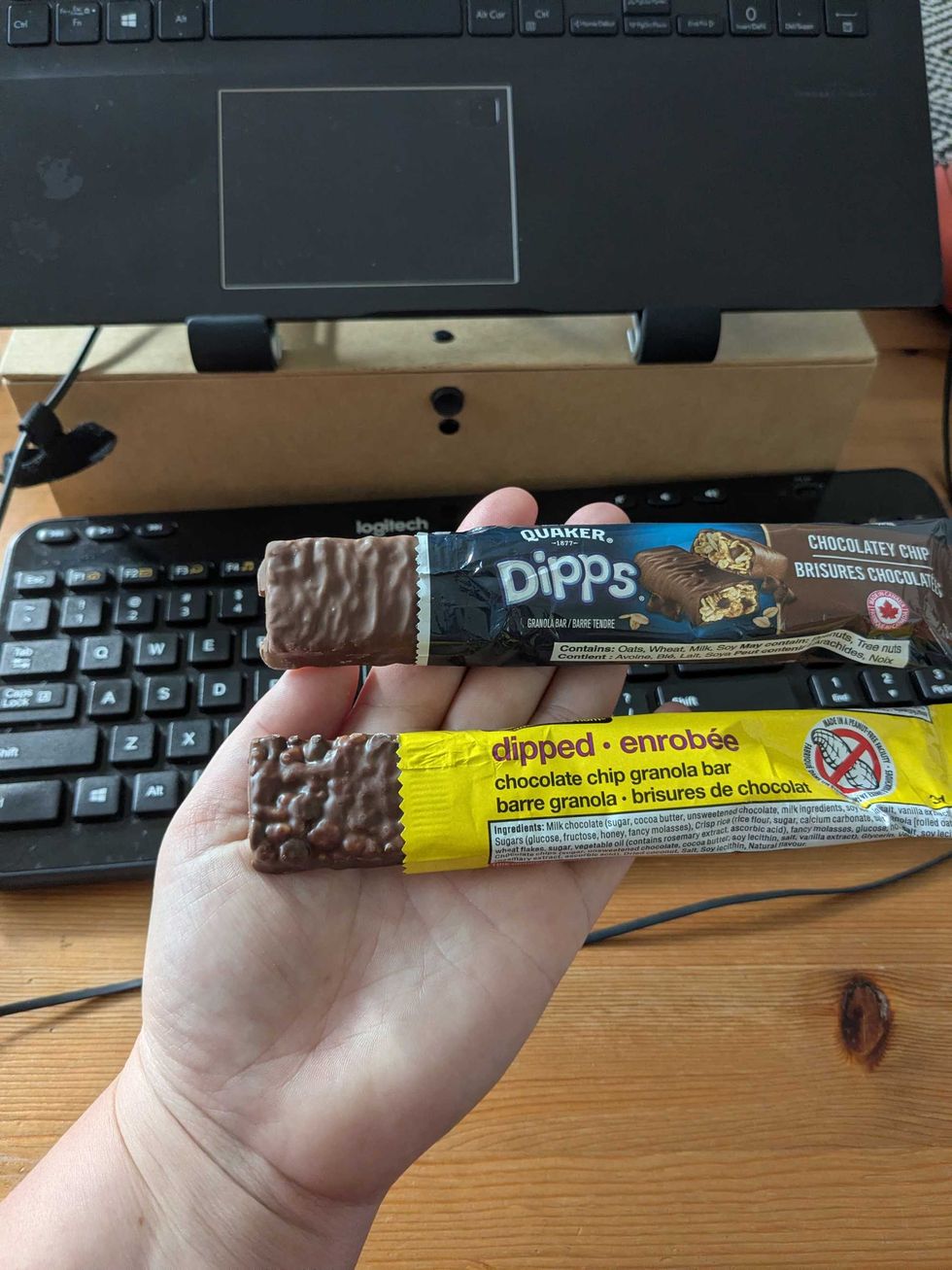 Someone holding two granola bars in their hand with the bar partially out of the wrapper