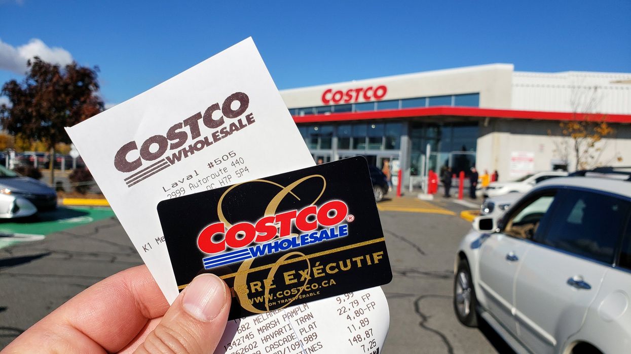 Someone holding up a Costco membership card and receipt in front of a Costco warehouse.