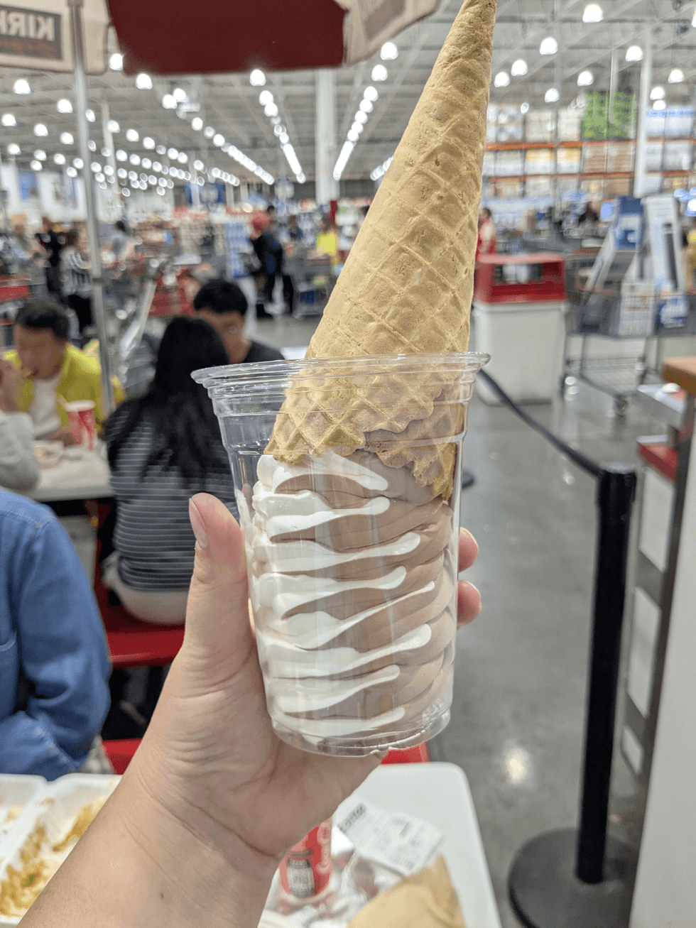 Someone holding up a vanilla chocolate swirl ice cream cone upside down in a cup at Costco