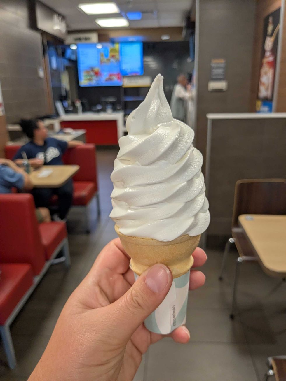 Someone holding up a vanilla ice cream cone at McDonald's