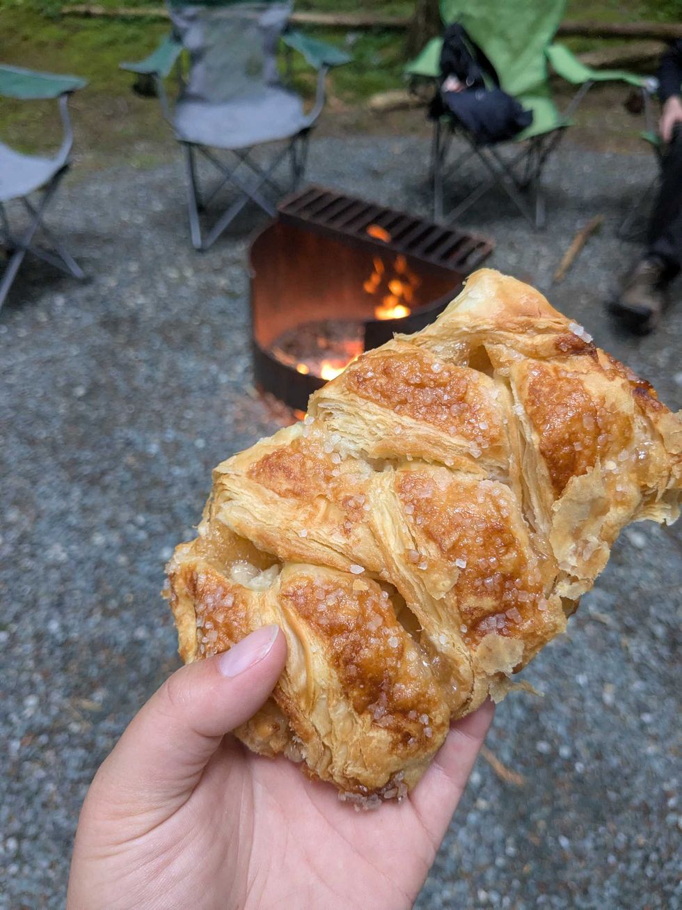 Someone holding up an apple turnover pastry in front of a campfire