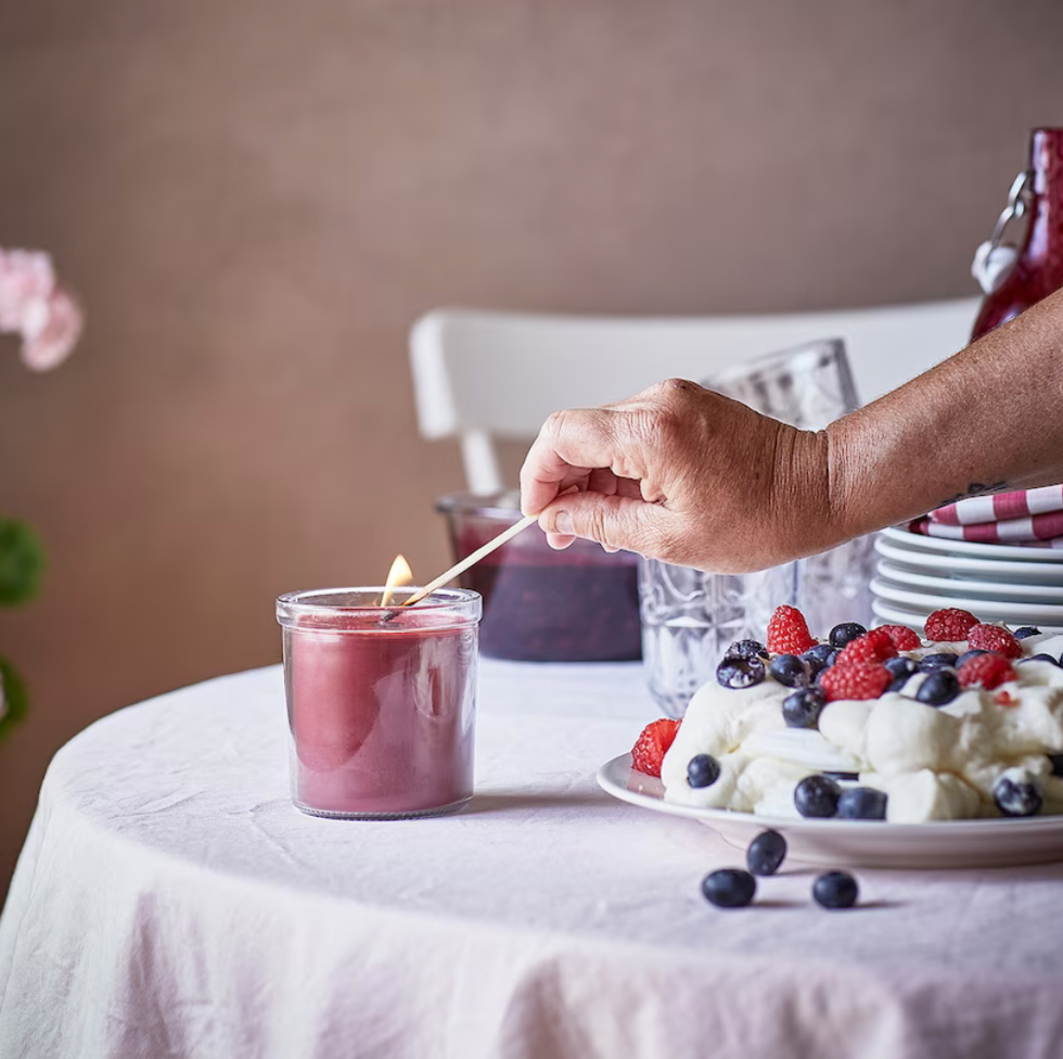 Someone lighting a red jar candle with a match.
