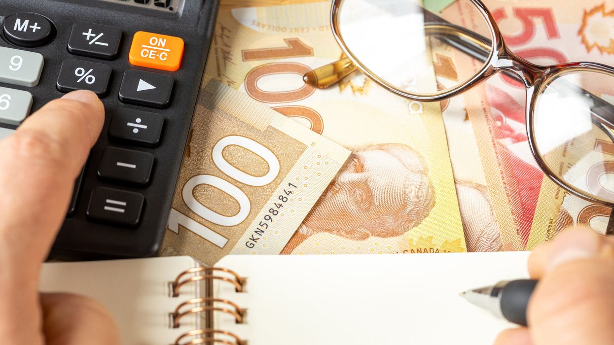 Someone using a calculator and notebook with Canadian money in the background.