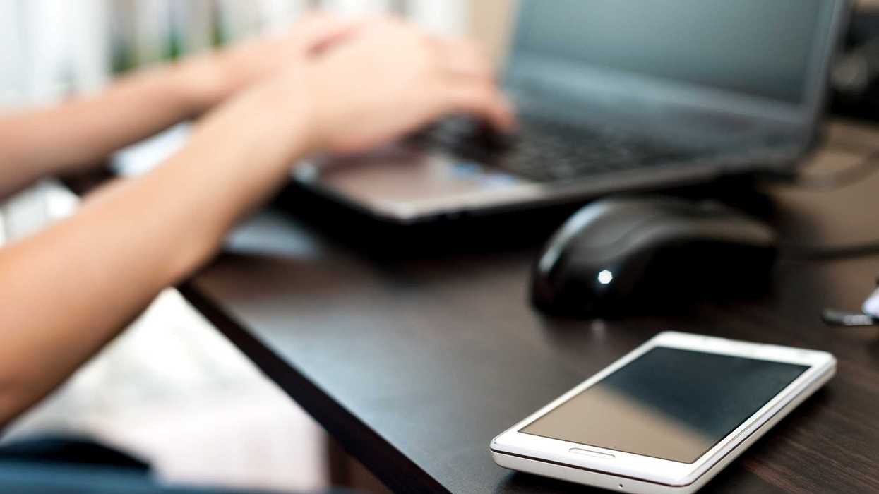 Someone using a computer, with a mobile phone in the foreground.