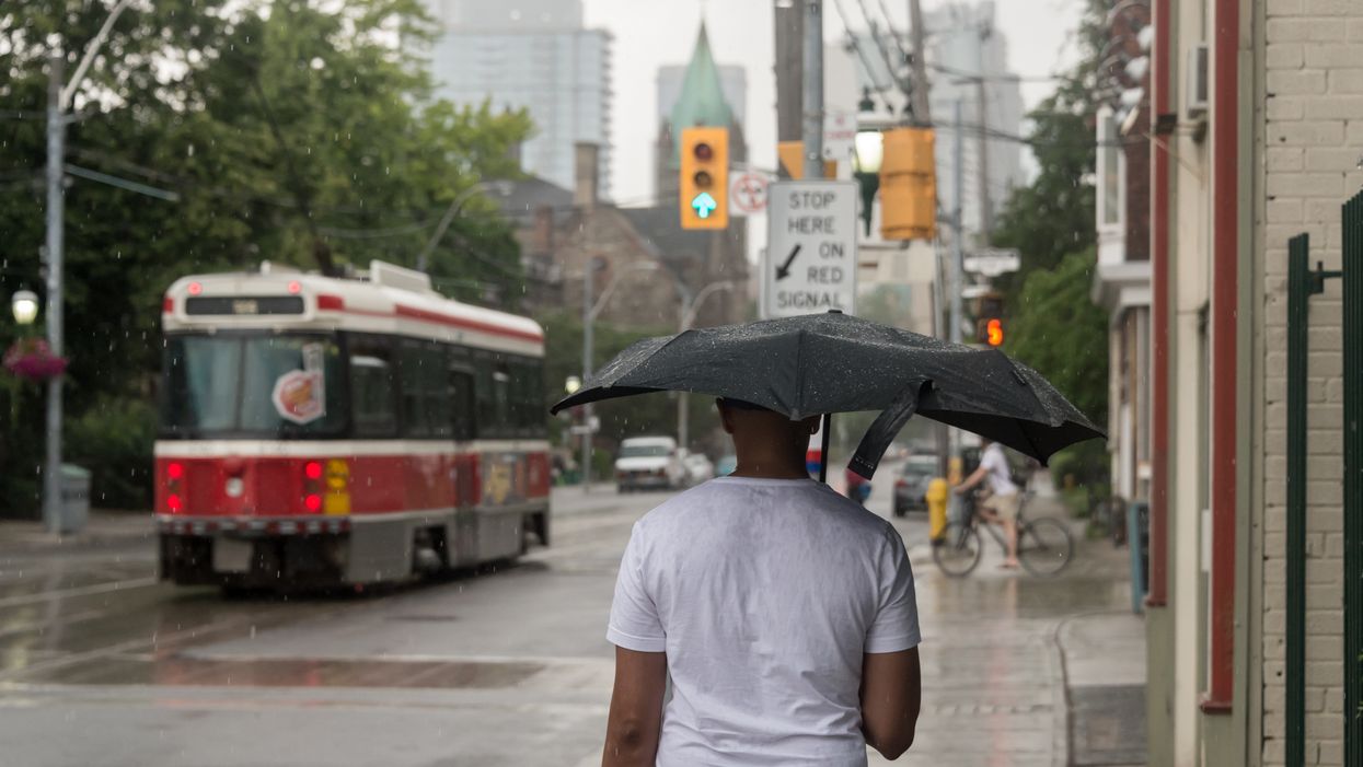 Someone walks down the street with an umbrella when it rains while a streetcar passes by.