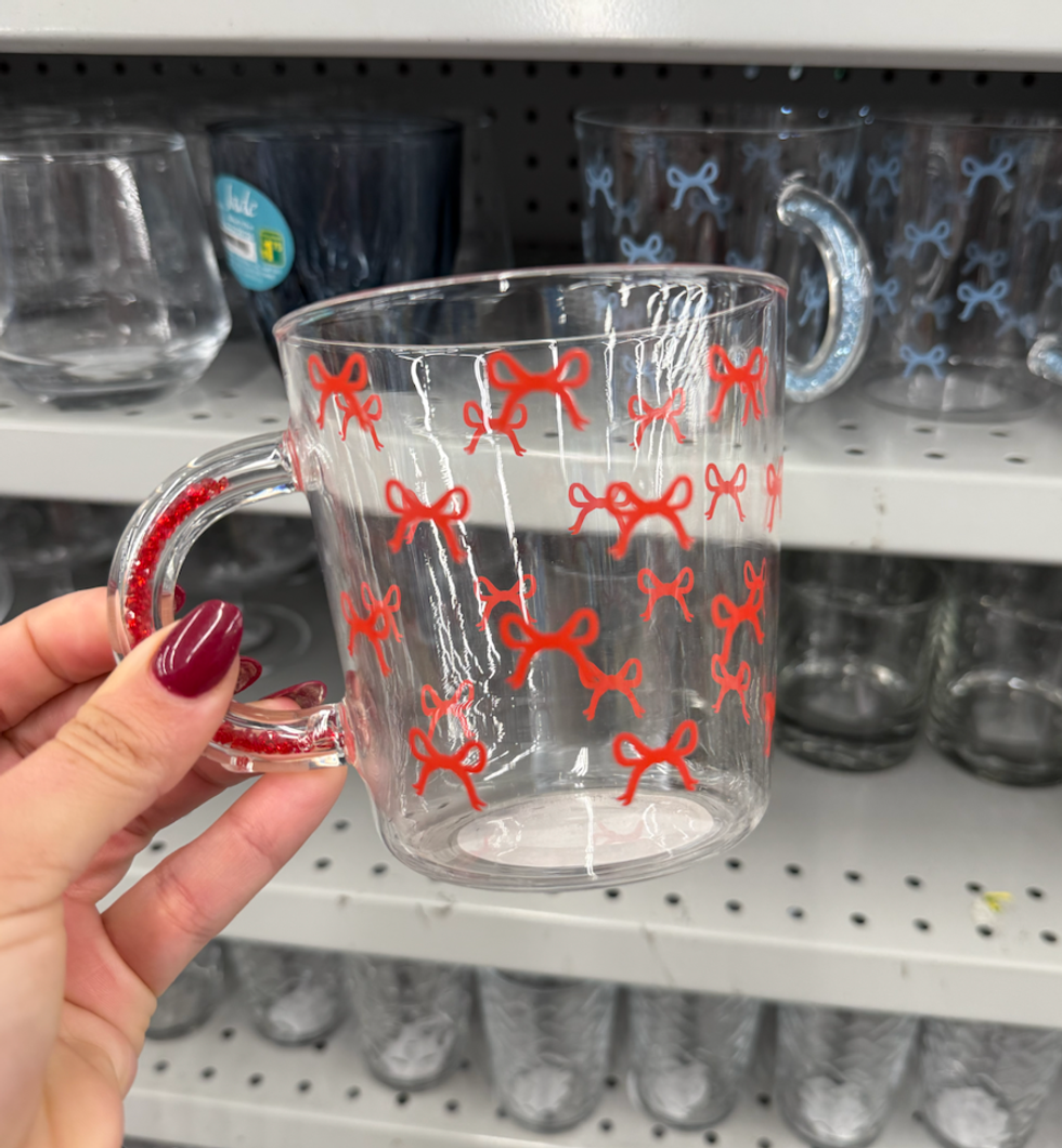 Tasse en verre transparente d\u00e9cor\u00e9e de petites boucles rouges tenue \u00e0 la main dans une all\u00e9e Dollarama.