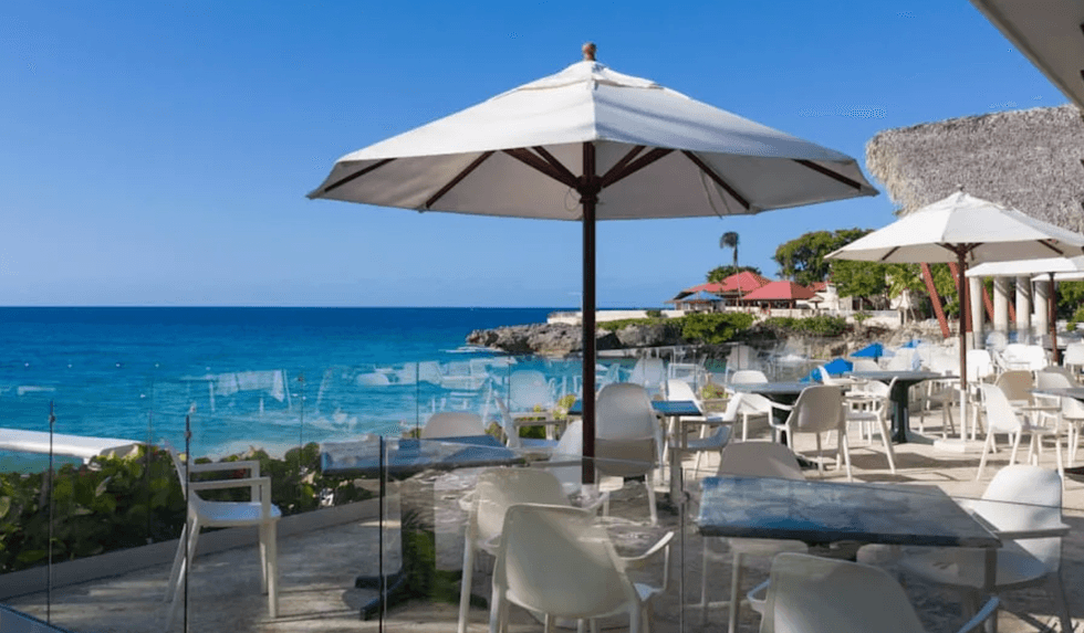 Terrasse avec tables et parasols blancs donnant sur la mer turquoise et les formations rocheuses au Casa Marina Sosua.