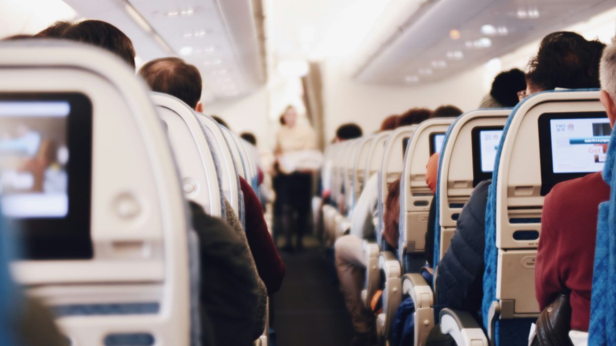 The aisle of an airplane is seen with seats filled with passengers on either side.