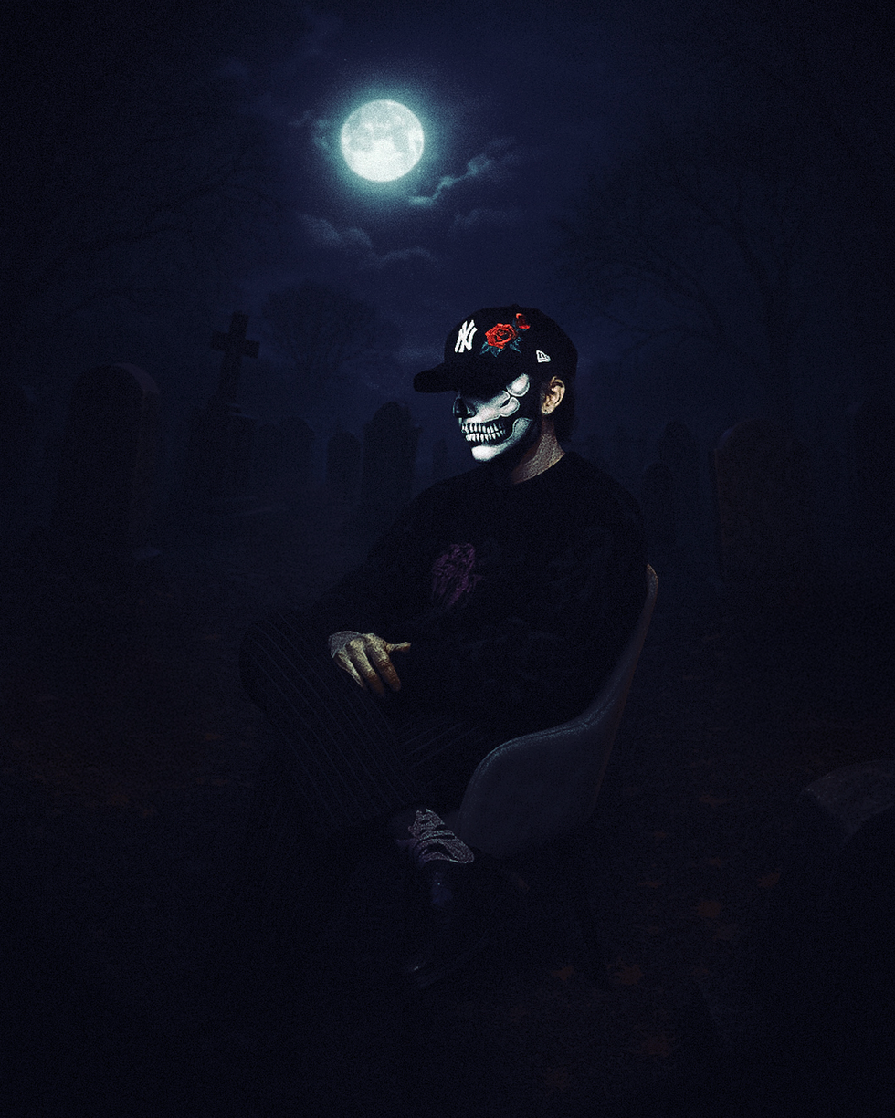 The artist Talwiinder, wearing face paint depicting a white skull and a New York Yankees baseball cap decorated with a red rose, sits in a chair moodily in front of a full moon.